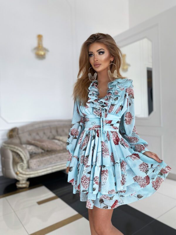 Close-up of the Sophia Mint Blue Floral Mini Day Dress showcasing its ruffled neckline, delicate floral pattern, and flowing layers in a luxurious room setting.